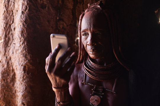 Old Himba woman checking her smartphone, Oncocua, Angola