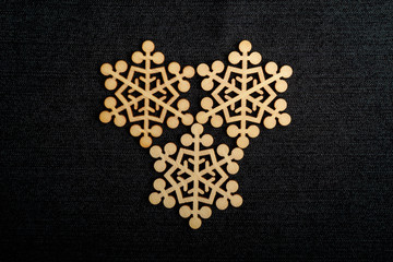 Three delicate light brown wooden snowflakes on dark grey textile material background, displayed on centre, top view with space for text around, flat lay with laser cut wooden objects, selective focus