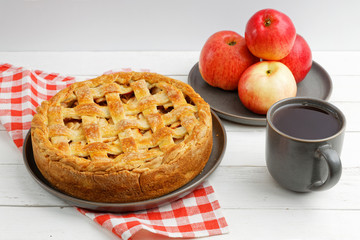 Homemade apple pie with lattice, apples and cup of tea on white wooden table. Angle view