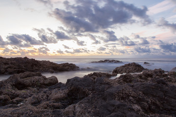 Fototapeta na wymiar mar adentrándose en rocas volcánicas en larga exposición con nubes al atardecer