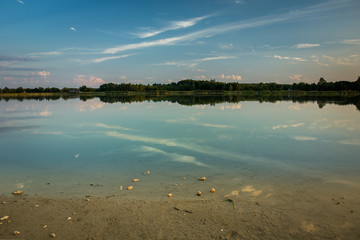 Sandy shore of a calm lake, reflection of cloud in water, evening view