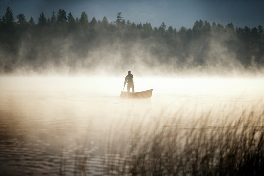 man standing in canoe in foggy lake