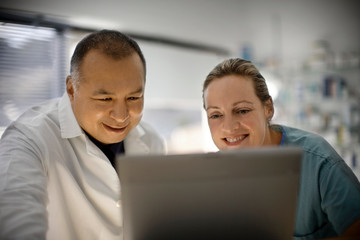 A doctor with a co worker smile while looking at the laptop.