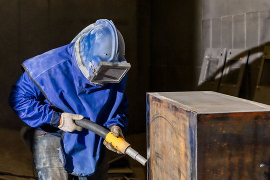 The operator of the sandblasting machine is ready to go. The worker is wearing a safety helmet and mask.