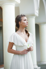 Young elegant woman with wedding bouquet in a light long white dress  before ceremony