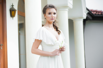 Young elegant woman with wedding bouquet in a light long white dress  before ceremony