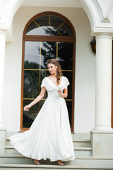 Fototapeta premium Beautiful young woman walking in long white dress. Tender bride with wedding bouquet.
