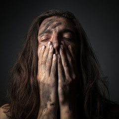 Fototapeta premium Portrait of a unhappy young man in soot. Hands on face
