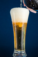 Full narrow glass of beer with foam on a blue background
