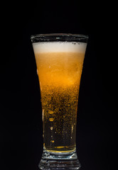 Glass of beer with foam on a black background in the dark