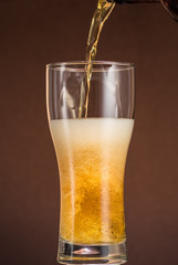 Full narrow glass of beer with foam on an orange brown background