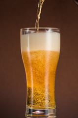 Full narrow glass of beer with foam on an orange brown background