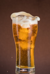Full narrow glass of beer with foam on an orange brown background