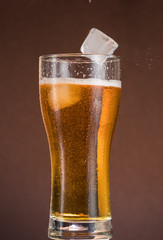 Full narrow glass of beer with foam on an orange brown background