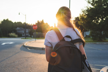 Profile of a teen girl depressed/sad at sunset in a parking lot while wearing a backpack and...