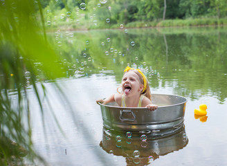 Excited girl sitting in tub and sticking out tongue at lake. Happy little kid having fun at summer vacations. Summer, childhood, vacations