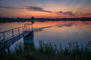 Lake bridge, colorful clouds on the sky after sunset, reflection of clouds in water