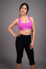 Young beautiful Asian woman ready for gym against gray backgroun