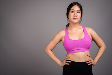 Young beautiful Asian woman ready for gym against gray backgroun