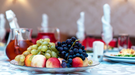Wedding. Event. Banquet. Decorated festive table with plates and glasses, beautiful white napkins. A plate of grapes, apples and peaches. Decanters with Morse red.