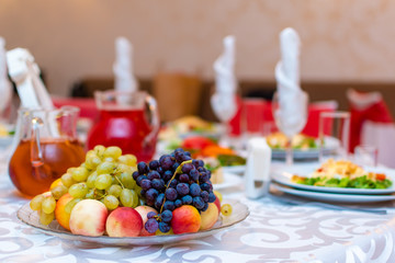 Wedding. Event. Banquet. Decorated festive table with plates and glasses, beautiful white napkins. A plate of grapes, apples and peaches. Decanters with Morse red.