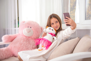 Shot of a younge girl sitting on the sofa at home and taking a selfie on the phone with soft toys