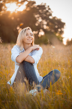 Young beautiful woman sitting on grass and smiles at sunset