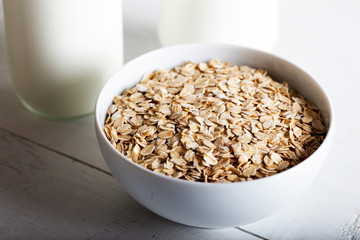Rolled oats or oat flakes in bowl with bottle of milk on white background.
