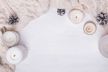 Knitted sweater or scarf, candles and pine cones on white bakground.