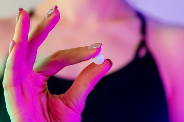 Woman's hand close-up holding drug pill in neon light