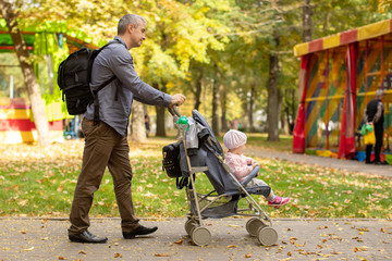 Man with baby stroller walks in the autumn park at sunset
