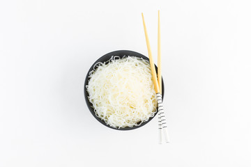 Cellophane rice noodles in a black bowl with chopsticks on white background, isolate, top view