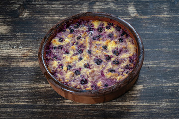 Sweet cottage cheese casserole with black currant and semolina on wooden table. Ceramic bowl with baked cottage cheese casserole