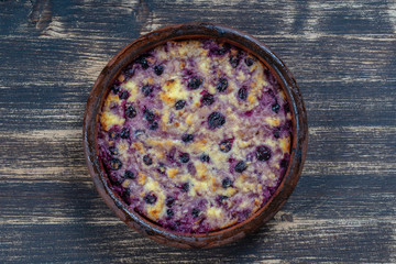 Sweet cottage cheese casserole with black currant and semolina on wooden table. Ceramic bowl with baked cottage cheese casserole