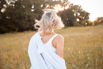 Fototapeta na wymiar Young woman in shirt walking outdoors under sunset light. Back