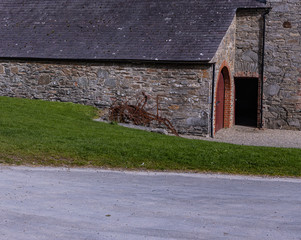 Rusty old farming machinery against a stone walled building with red door