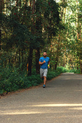 Young active handsome male healthy runner jogging outdoors along a scenic path in a forest. Vertical shot.