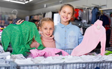 Two small happy sisters satisfied with purchases in children clothing shop