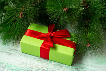 A wrapped green gift with a red ribbon lies under a Christmas tree on a wooden floor