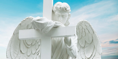 Angel with cross against blue sky. Ancient statue.