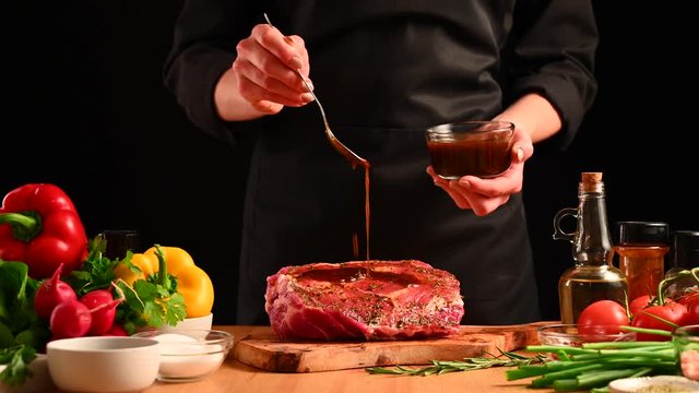 Chef cooks pork ribs. sprinkling with pepper on a background with vegetables. Freezing in motion. Recipe book, cooking, restaurant business