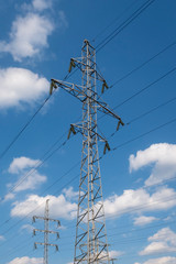 2 electricity power poles and white clouds on blue sky. Energy supply.