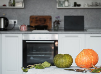 Two pumpkins on the kitchen white table. Near autumn leaves. The second is the kitchen. Cooking. Harvesting. Close-up. Light background. Halloween Autumn.