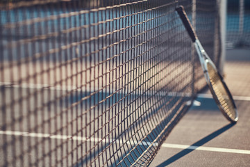 Tennis racquet is standing near tennis net outside at bright sunny day.