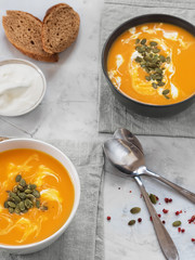 Two bowls with pumpkin soup, sauce and pumpkin seeds on a gray linen napkin. Sauce, bread and pumpkin seeds. Light background. Seasonal dish. Halloween. Top view.