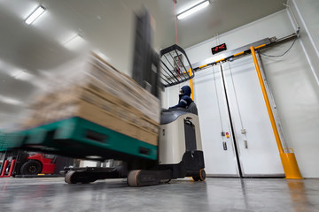 Worker Stand-on stacker truck used to lift and move the ready meals goods stock in cold room or...