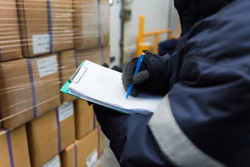 Closeup shooting hand of worker with clipboard checking goods in freezing room or warehouse.,Import...