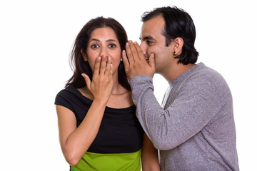 Studio shot of Persian couple with man whispering to woman looki