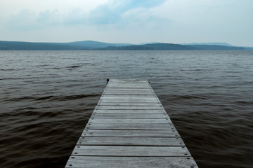 Fototapeta na wymiar An Old Wooden Dock Jutting Out Into A Dark And Gloomy Lake With Cold Water