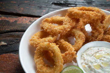 Fried calamari rings with dip sauce isolated on rustic wooden table